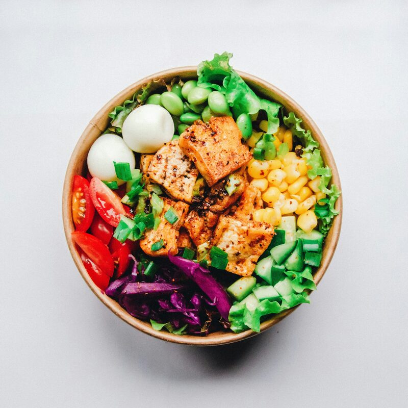 A tofu rice bowl with edamame, corn, tomatoes, cucumber and red cabbage