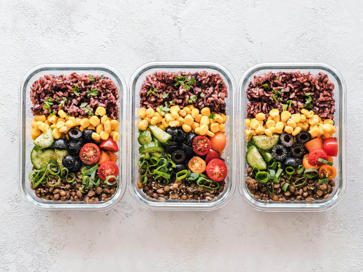 Three packed lunchboxes of rice, vegetables and eggs, lined up on a table.