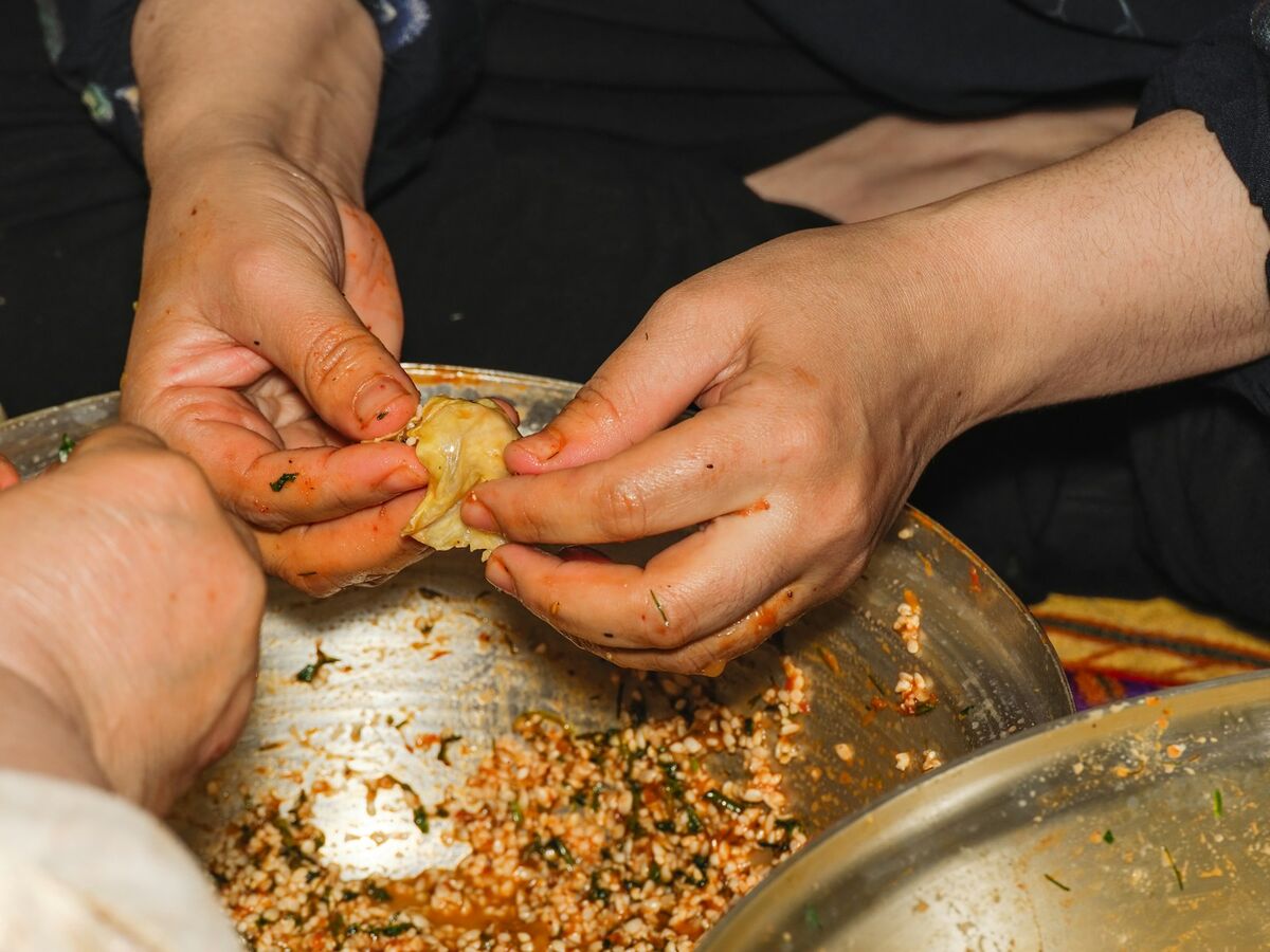 Two pairs of hands roll rice filling into leaves over a large metal bowl.