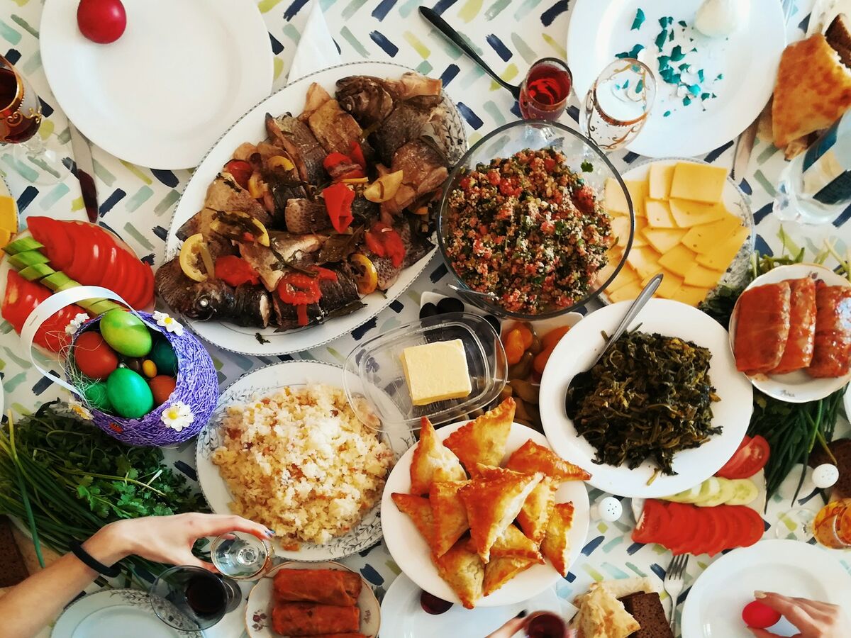 Many dishes fill a patterned tablecloth seen from above, including kebabs, salads, pastries and cheese.