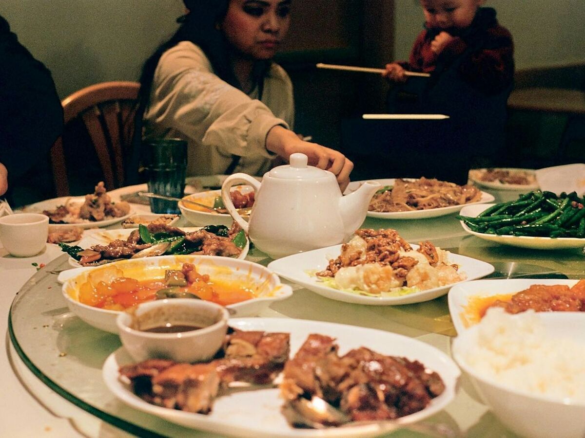 Friends reach across a round table with a lazy susan full of shared dishes and a teapot.