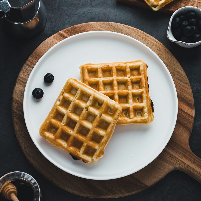 Two golden waffles on a white plate with blueberries and syrup