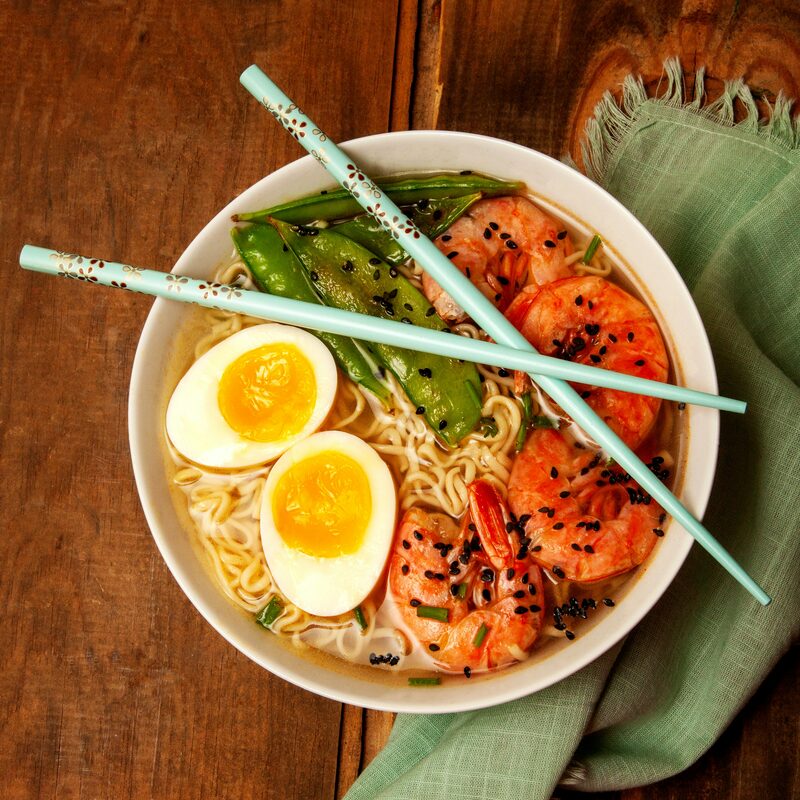 A bowl of ramen topped with soft-boiled eggs, salmon, avocado and chopsticks