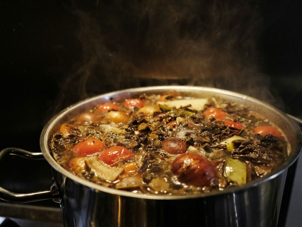 A large steel pot of vegetable soup steams on the stove.