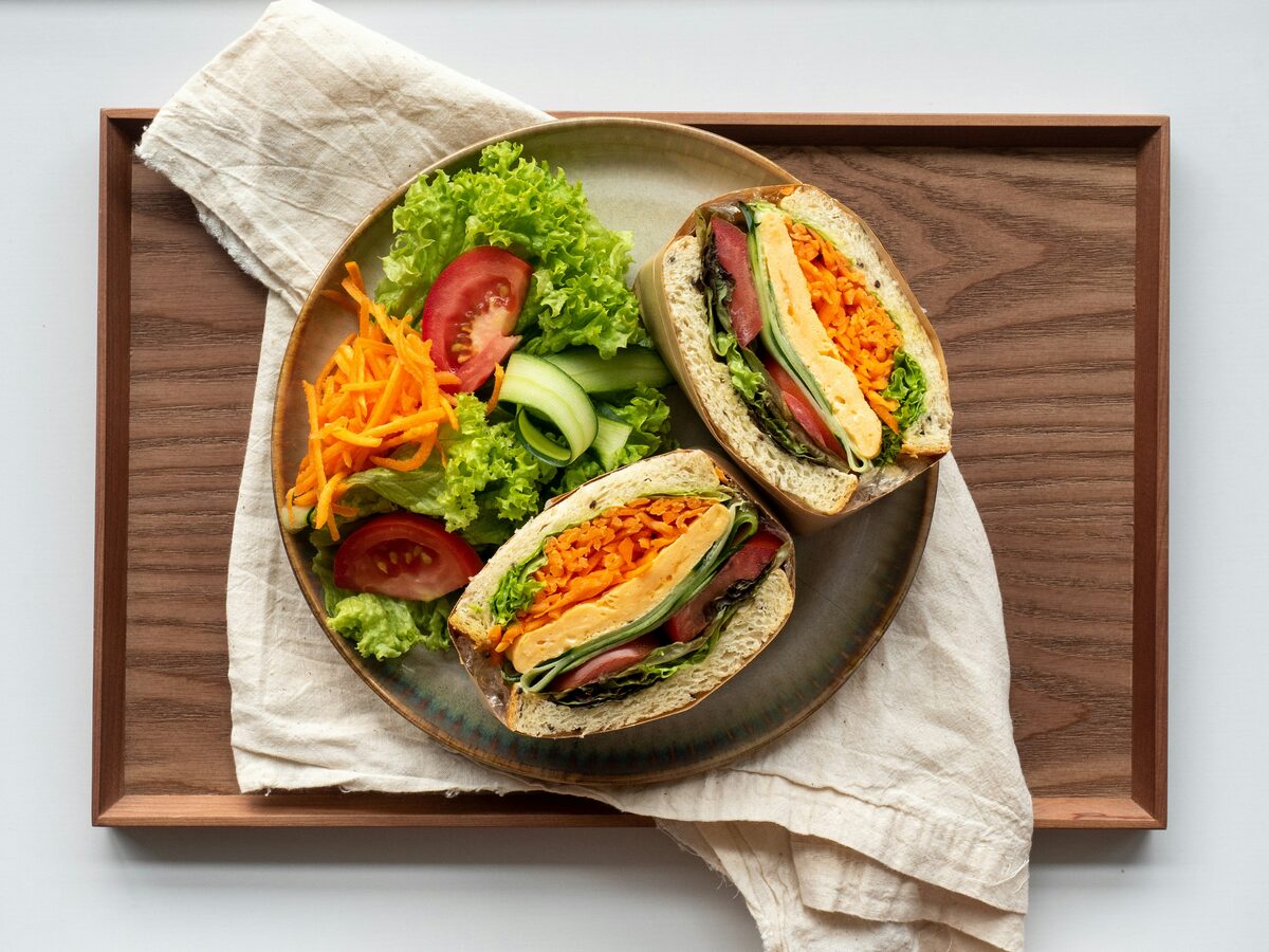 A sandwich with omelette, carrot and lettuce, halved on a plate with salad, on a wooden tray
